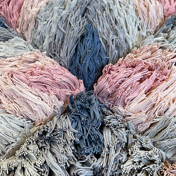 Detail photo of a pink and blue ceramic sculpture of a geometric patterned shag rug by Risa Hricovsky.