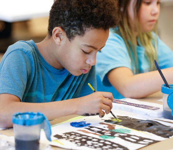 Photo of a young boy painting with watercolors in an art class.
