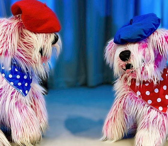 Photo of two pink dog puppets wearing bandanas and berets.