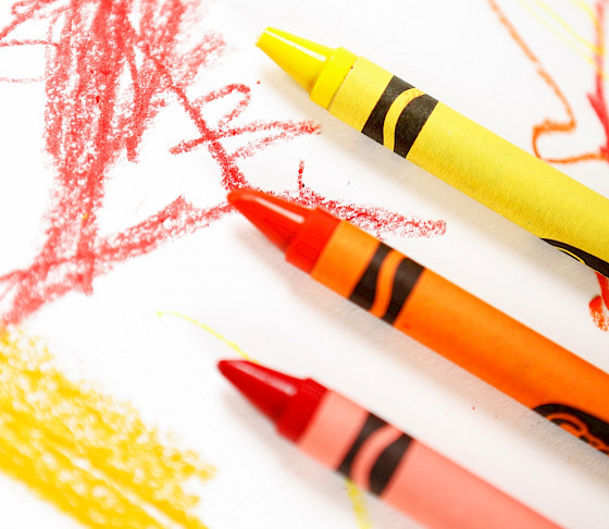 Close up photo of a red, orange, and yellow Crayon surrounded by scribbles on a white piece of a paper.