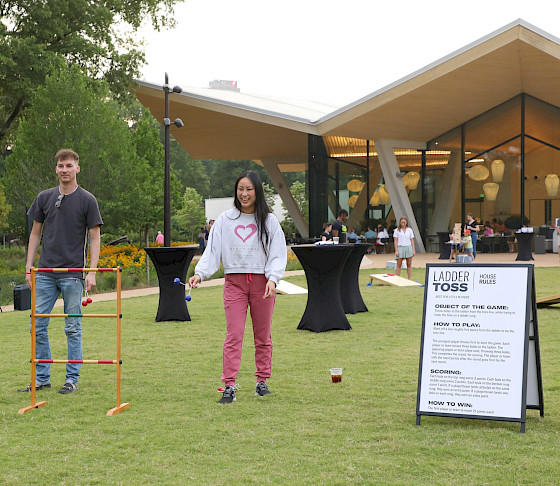 Photo of a man and woman playing ladder toss on the Event Lawn at AMFA while children in the background play cornhole.